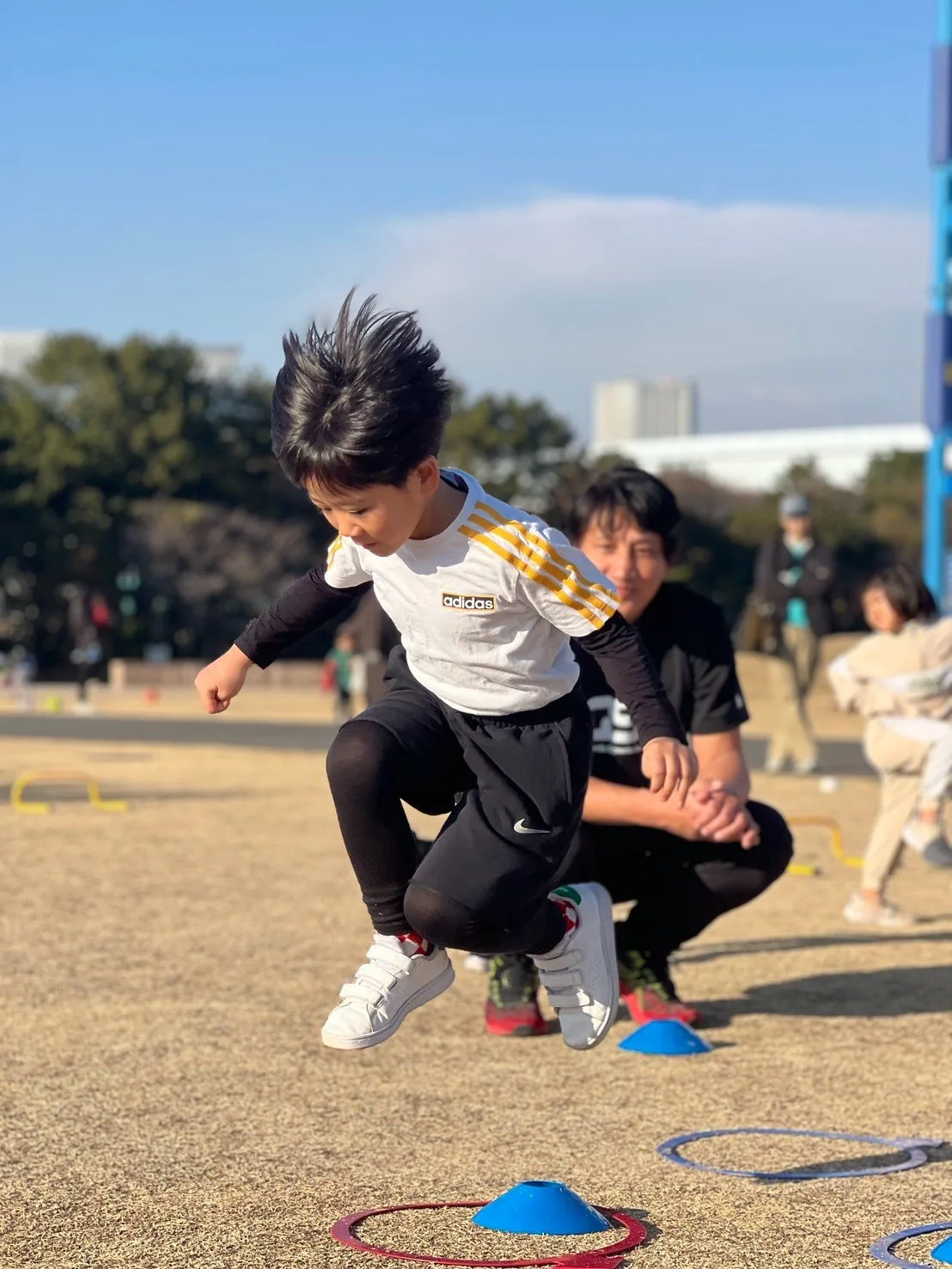 コーンを跳び越える男の子と、後ろで見守るコーチ