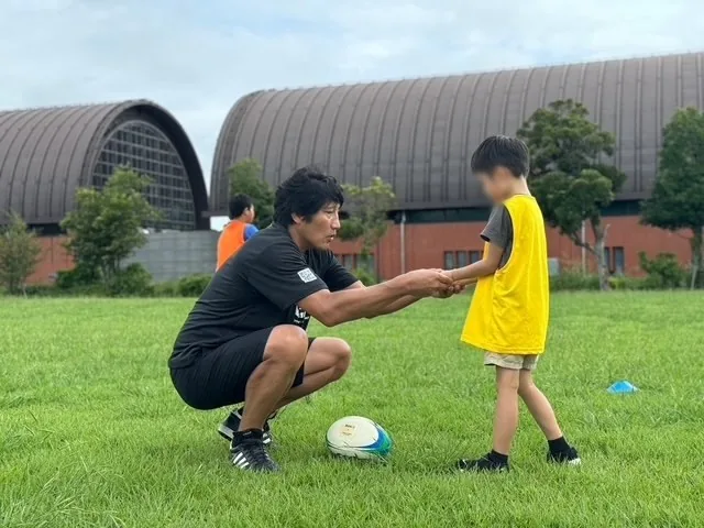 しゃがんで子どもと目線を合わせ、手を取るコーチ