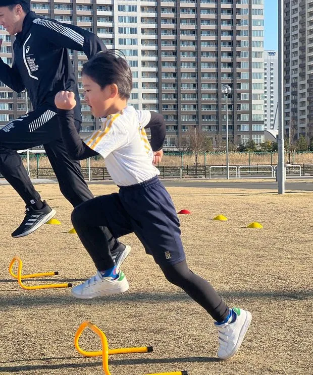 ミニハードルを走り越える子どもとコーチ